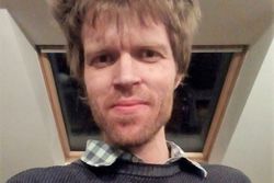 Dr Piotr Bakalarczyk. Mężczyzna w koszuli w jasną kratkę i swetrze, o bujnych i jasnych włosach.
