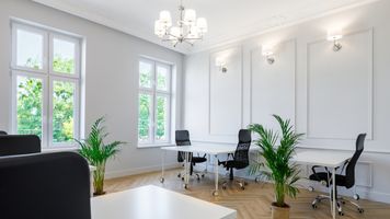 Miniatura Jasne, eleganckie biuro coworkingowe z dużymi oknami, sześcioma biurkami i czarnymi ergonomicznymi krzesłami. Wnętrze urządzone w klasycznym stylu z ozdobnymi panelami na ścianach, roślinami w doniczkach i lampami ściennymi oraz żyrandolem. Na podłodze jasny parkiet, za oknami widać drzewa.
