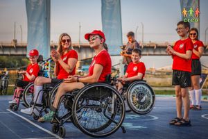 Miniatura Osoby poruszające się na wózkach i pełnosprawne biorą udział w zajęciach. Uśmiechają się i klaszczą. Wszyscy mają na sobie czerwone koszulki.