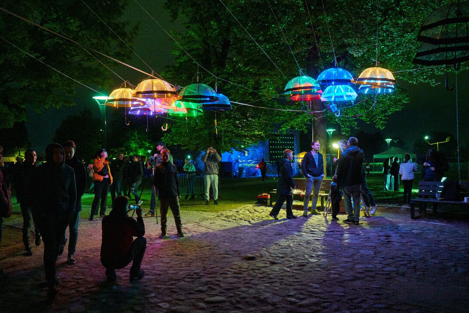 Uczestnicy spacerują wieczorem pod baldachimem z świecących na kolorowo parasolek