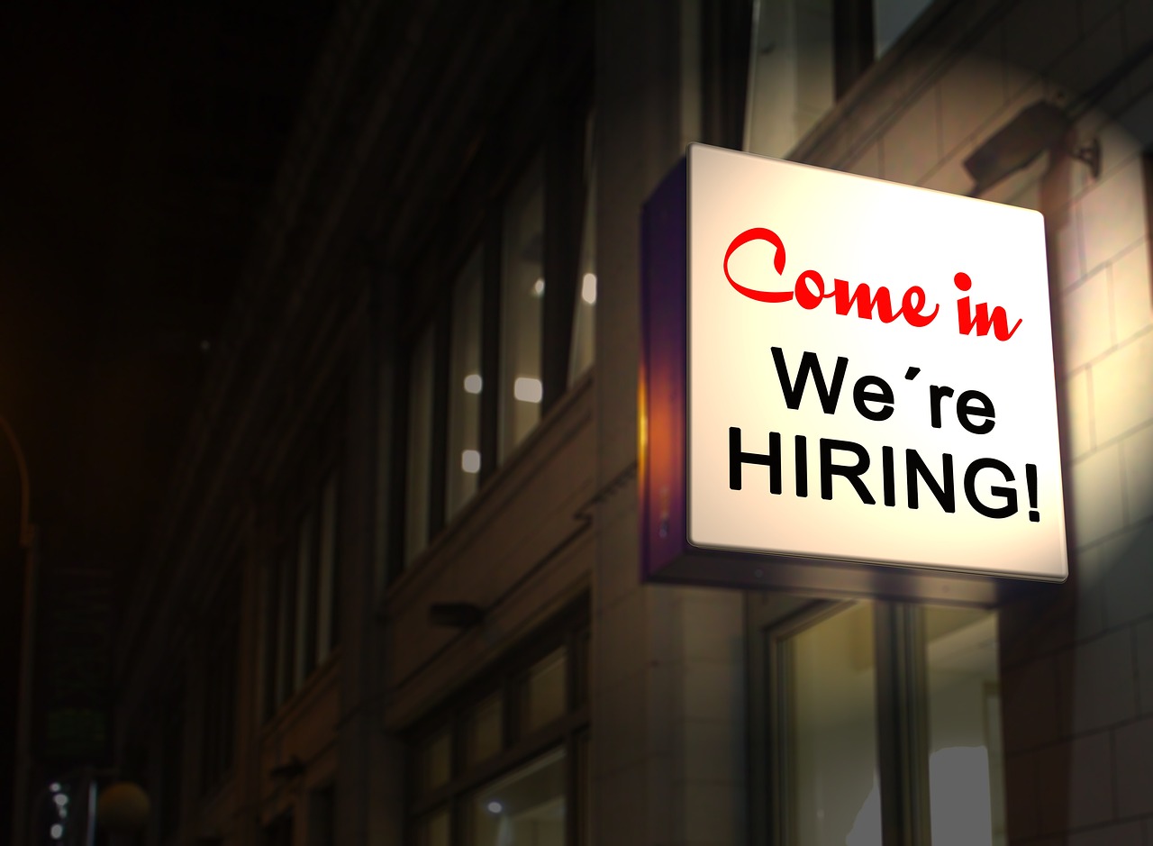 Zdjęcie budynku z neonem o treści: Come in. We're HIRING! [Chodź, praca czeka]