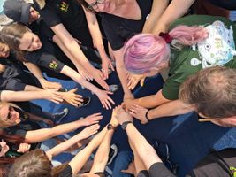 Miniatura Wolontariusze w czarnych koszulkach z logo CREO. Kładą dłoń na dłoni w geście współpracy.