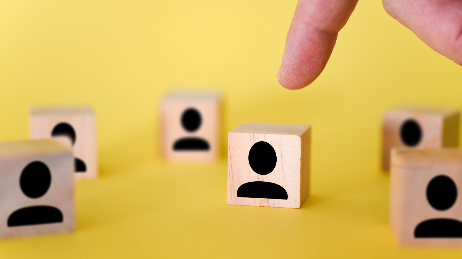 Zdjęcie przedstawia drewniane klocki z symbolicznymi rysunkami osoby. Na jeden z nich ktoś wskazuje pacem. 