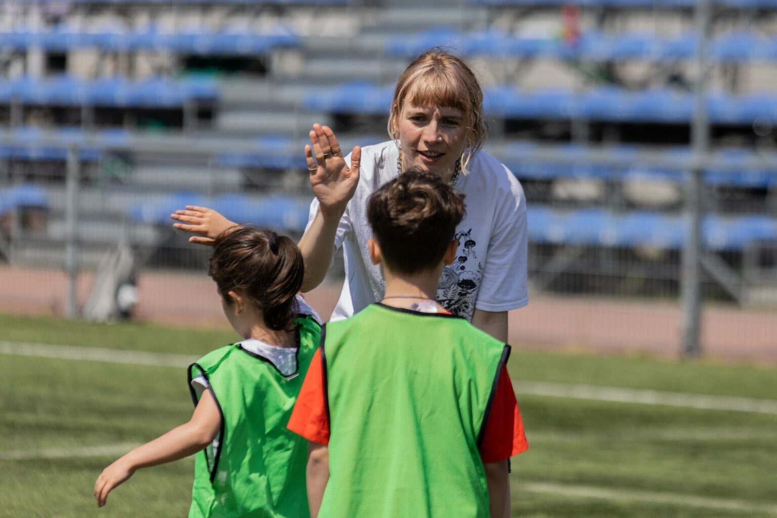 Etnoliga dla dzieci. Dziewczynka i chłopiec w strojach sportowych przybijają piątkę z wychowawczynią