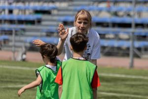 Miniatura Etnoliga dla dzieci. Dziewczynka i chłopiec w strojach sportowych przybijają piątkę z wychowawczynią