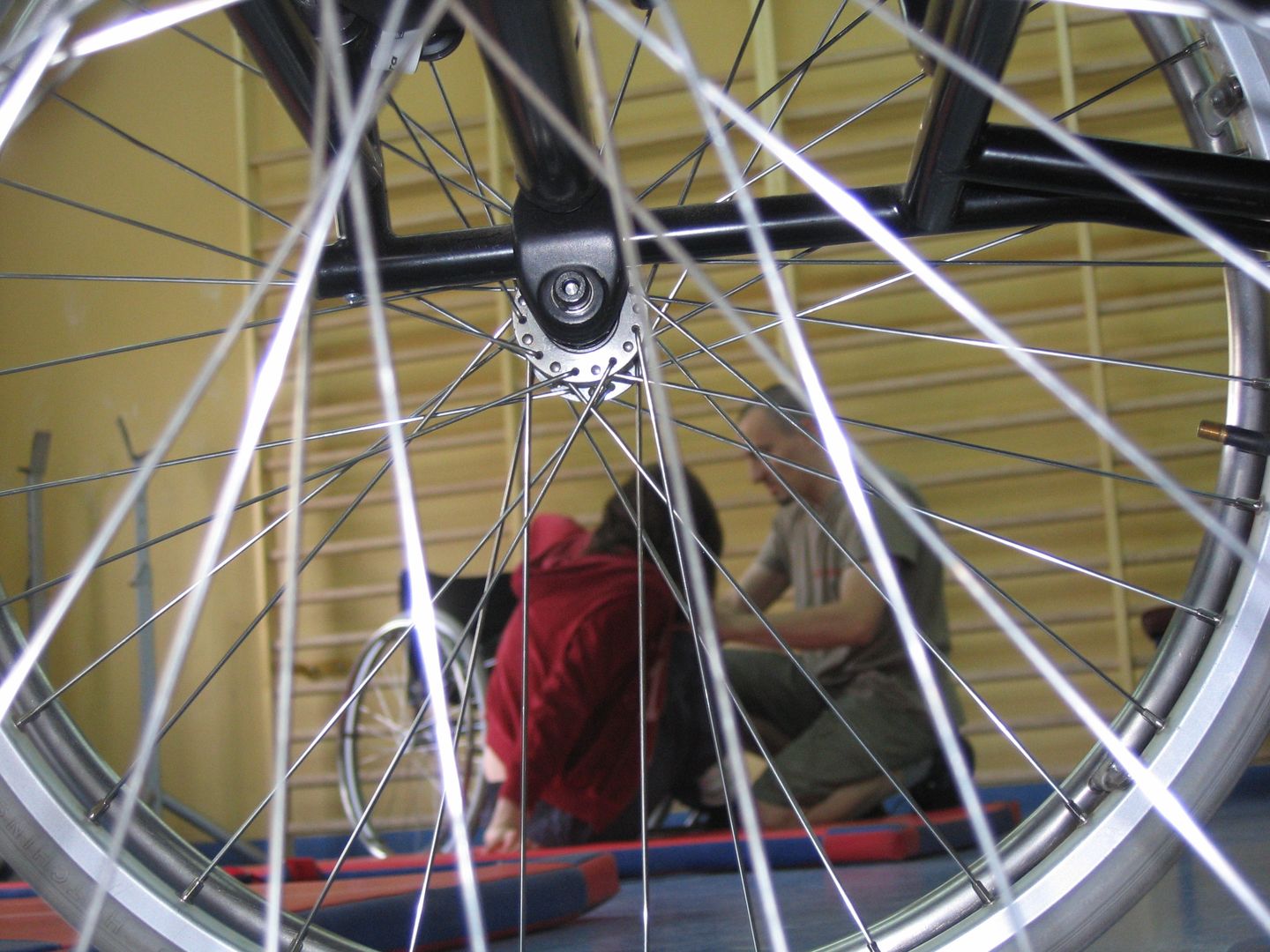 zdjęcie przedstawia osobe poruszająca sie na wózku w momencie ćwiczenia przesiadania sie na powierzchnie o różnej wysokości a askeuracją osoby chodzącej