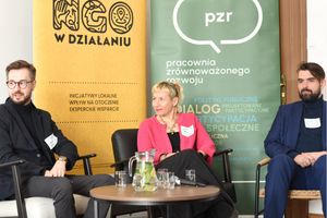 Miniatura Troje panelistów siedzi w fotelach podczas dyskusji. Przed nimi stoi mały stolik z dzbankiem wody, szklankami i mikrofonem. W tle widoczne są banery „NGO w działaniu” oraz „Pracownia Zrównoważonego Rozwoju (pzr)”.