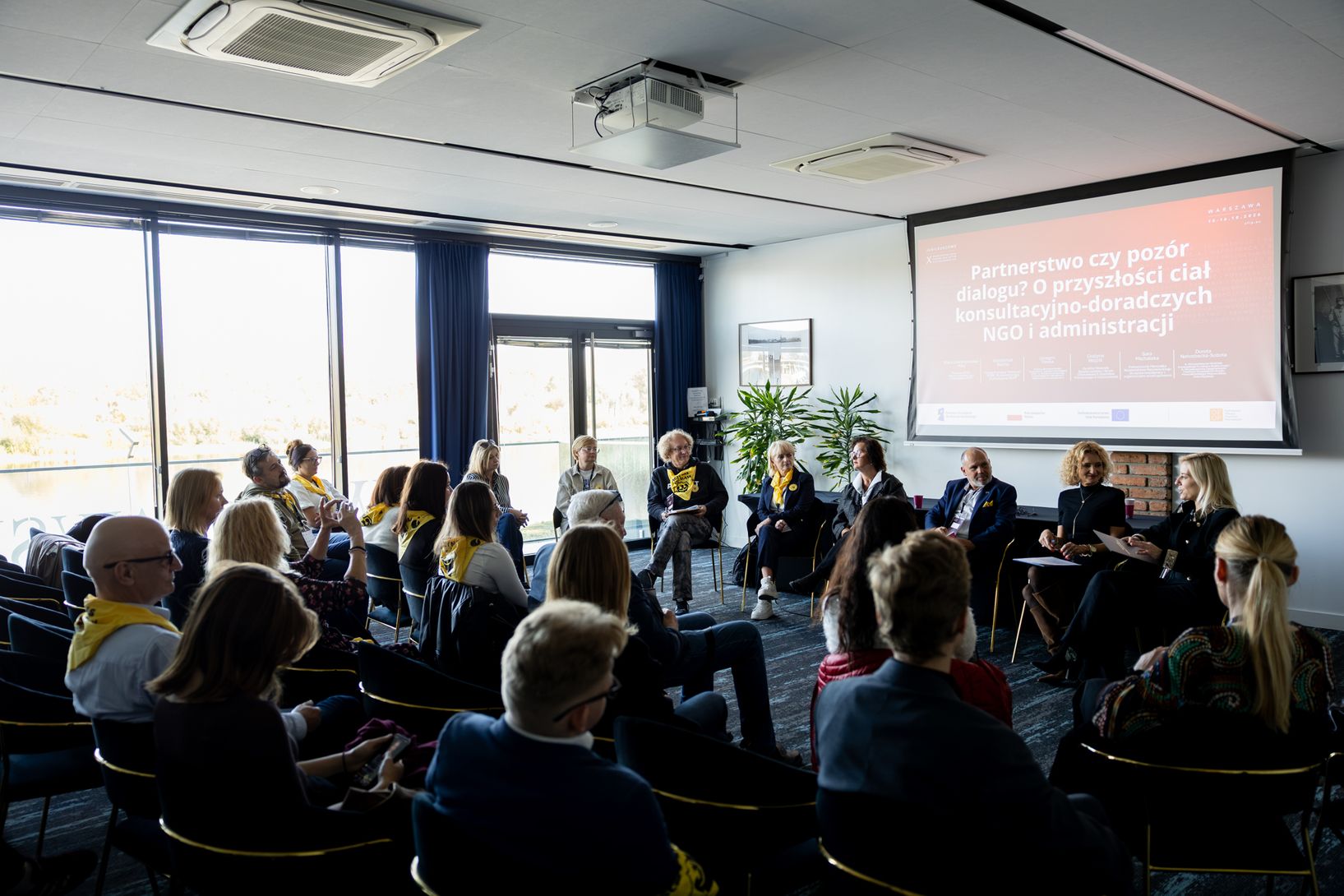 czestników oraz panelistów zgromadzonych w jasnej sali konferencyjnej, siedzących w okręgu podczas sesji warsztatowej lub panelu dyskusyjnego.